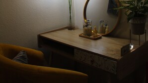 Een kamer met een bureau, een stoel, een spiegel, een potplant en hanglampen.