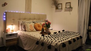 Een slaapkamer met een bed, nachtkastje, lamp en decoratieve elementen.