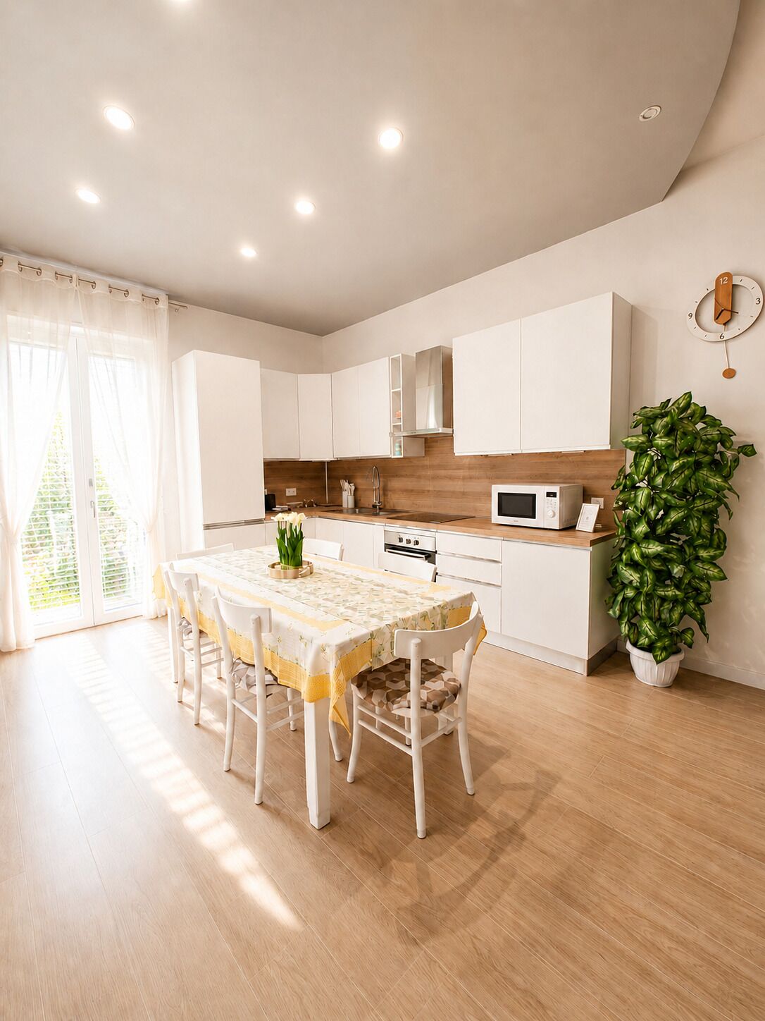 Une cuisine moderne avec des meubles blancs, un plan de travail en bois et un coin repas comprenant une table et des chaises.
