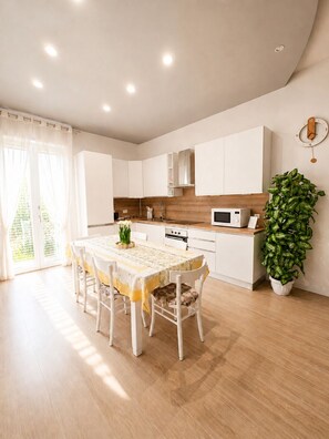 A modern kitchen with white cabinets, a wooden countertop, and a dining area with a table and chairs. - In DhomeU Tua (Selargius)