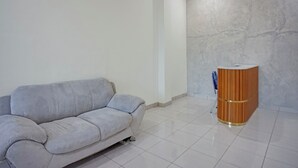 A room with a grey sofa and a wooden cabinet against a textured wall. - Hotel O near Universitas Sumatera Utara  (Medan)