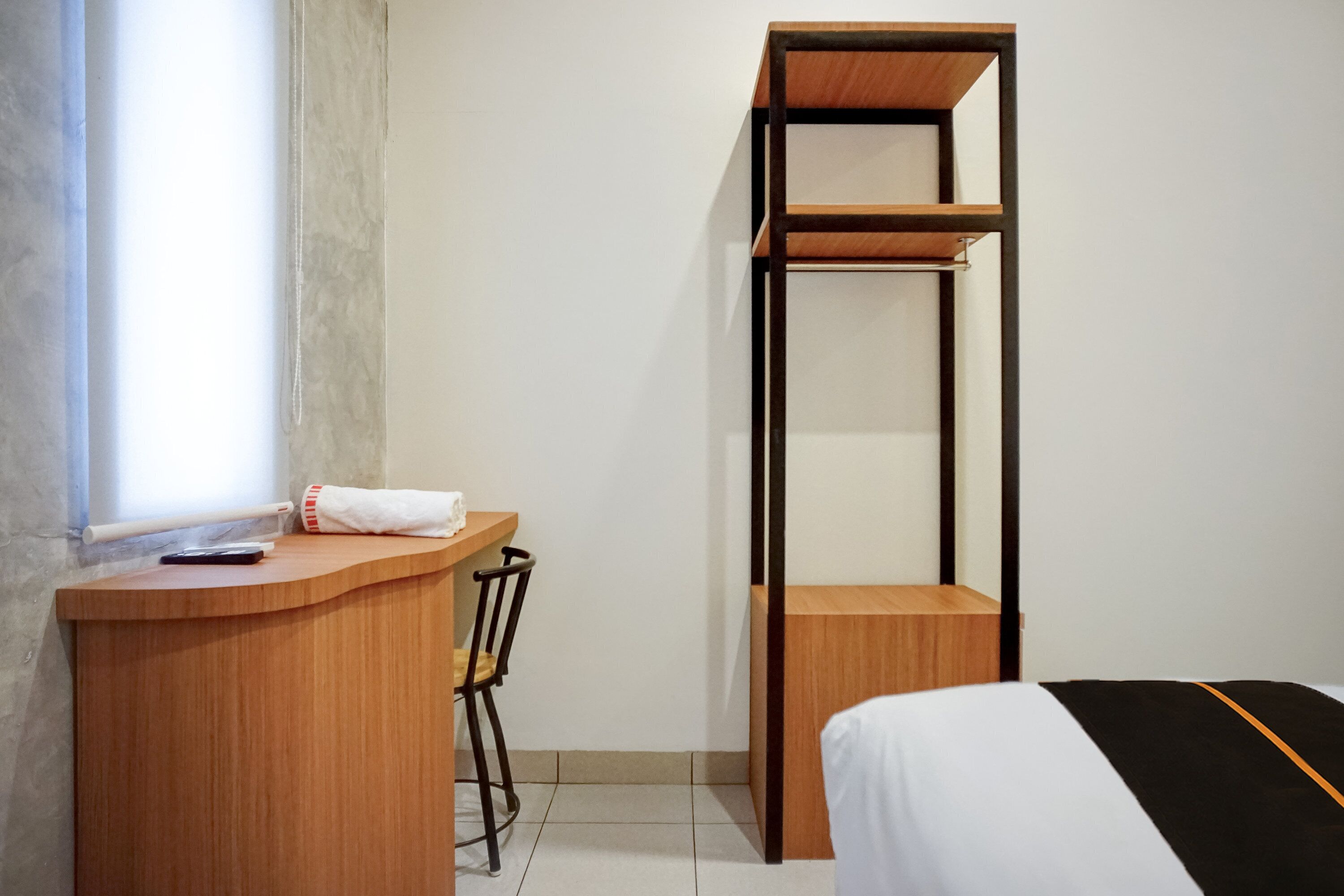 A compact room with a wooden desk, a chair, a bed, and a tall shelving unit.
