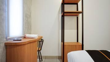 A compact room with a wooden desk, a chair, a bed, and a tall shelving unit.