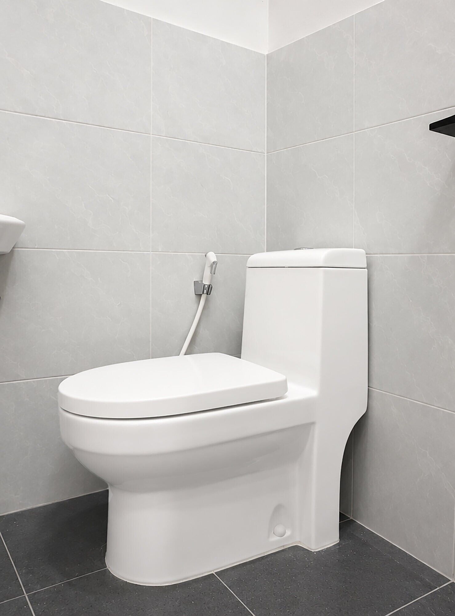 Un inodoro blanco en un baño con azulejos grises en las paredes y el suelo.