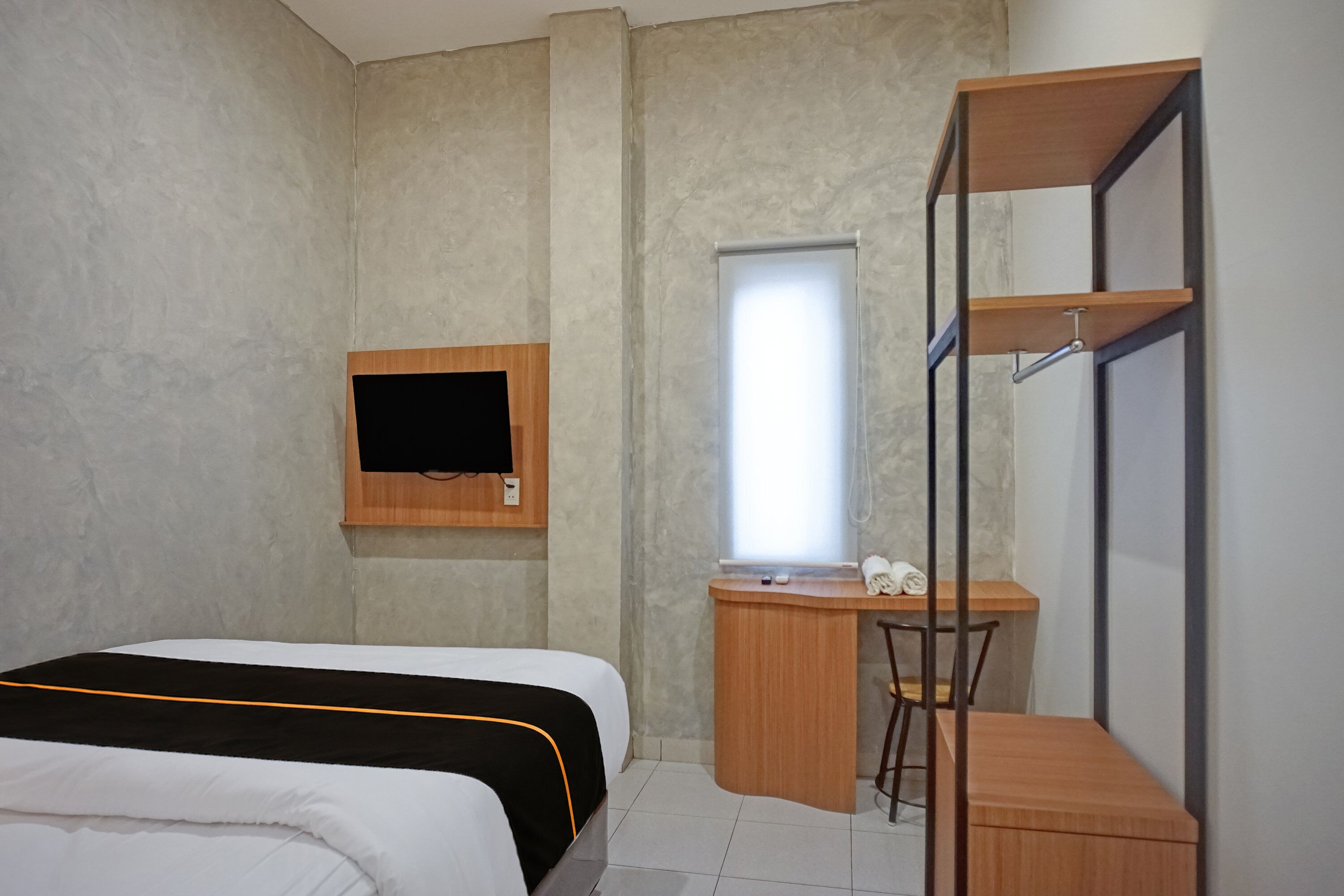 A compact hotel room with a bed, a desk, a chair, a TV mounted on the wall, and a window.