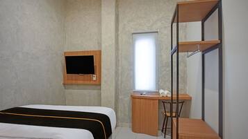 A compact hotel room with a bed, a desk, a chair, a TV mounted on the wall, and a window.