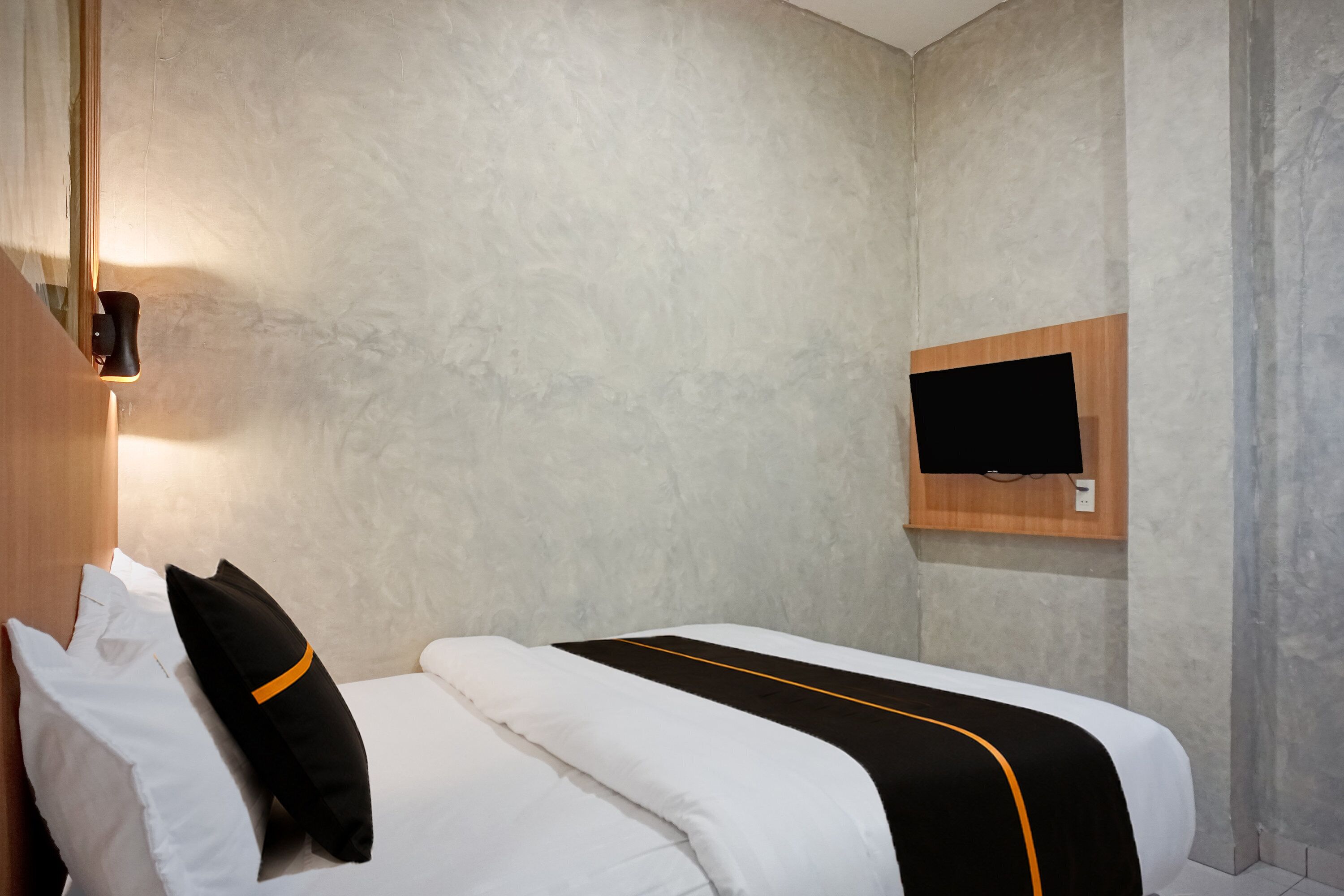 Ein Hotelzimmer mit einem Bett, Kissen, einem flachbildfernseher an der Wand und einem hölzernen Kopfteil.