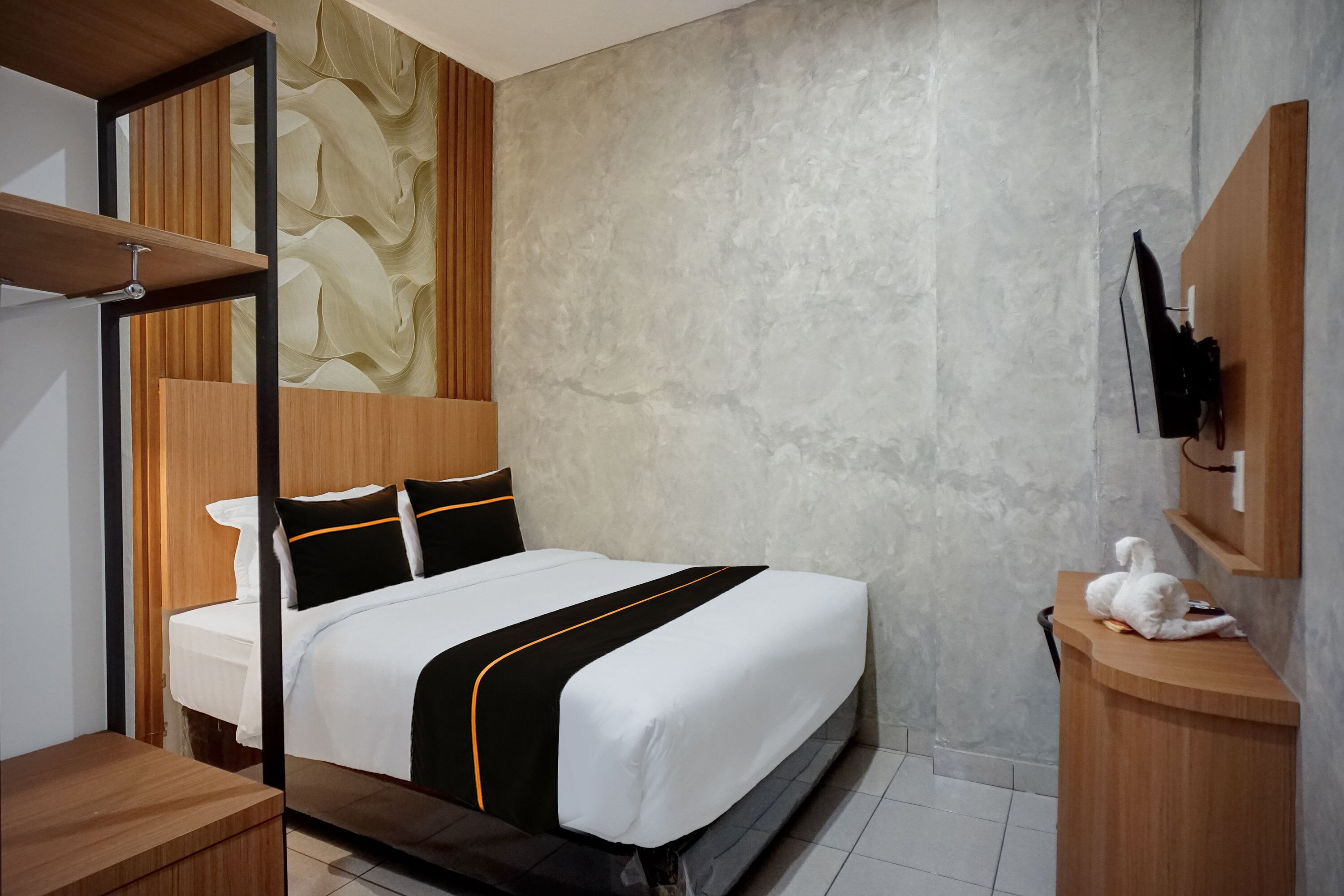Een moderne hotelkamer met een bed, een houten hoofdeinde en een aan de muur bevestigde televisie.