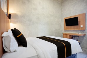 Una habitación de hotel con una cama, un escritorio y un televisor fijado a la pared.
