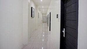 A corridor with white walls, a tiled floor, and a black door on the right. - Hotel O near Universitas Sumatera Utara  (Medan)
