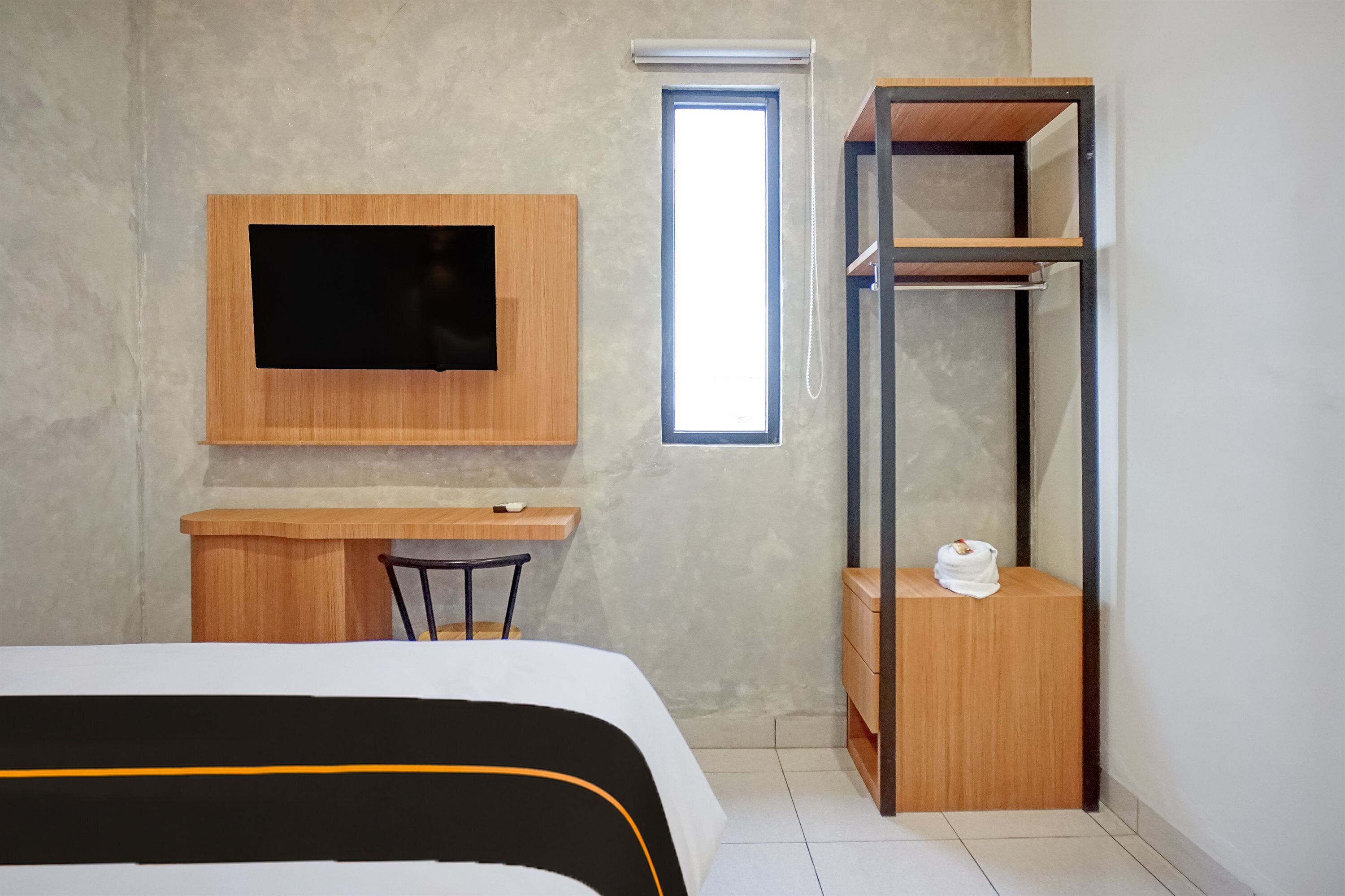 A compact hotel room with a bed, a desk, a TV mounted on the wall, and a window.