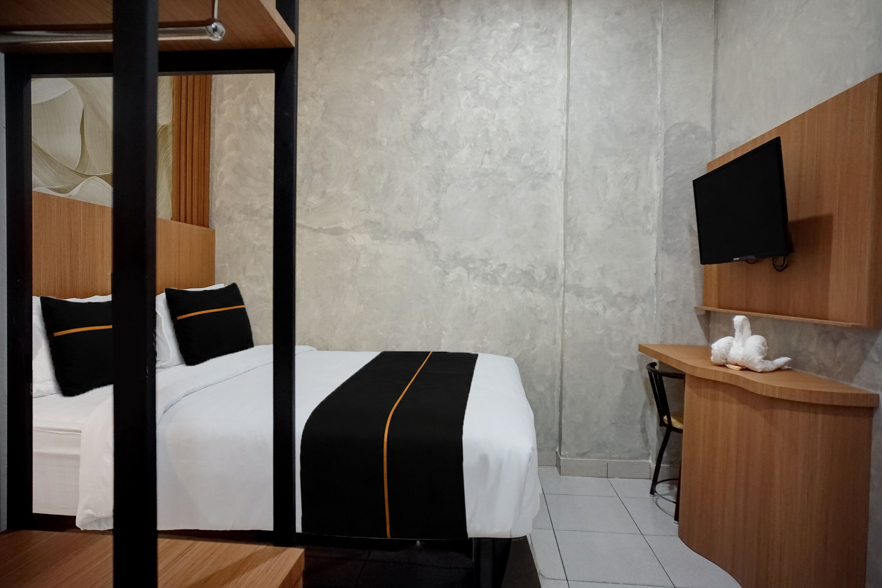 Une chambre d’hôtel équipée d’un lit, d’un bureau, d’une chaise, d’une télévision et d’une étagère fixée au mur.