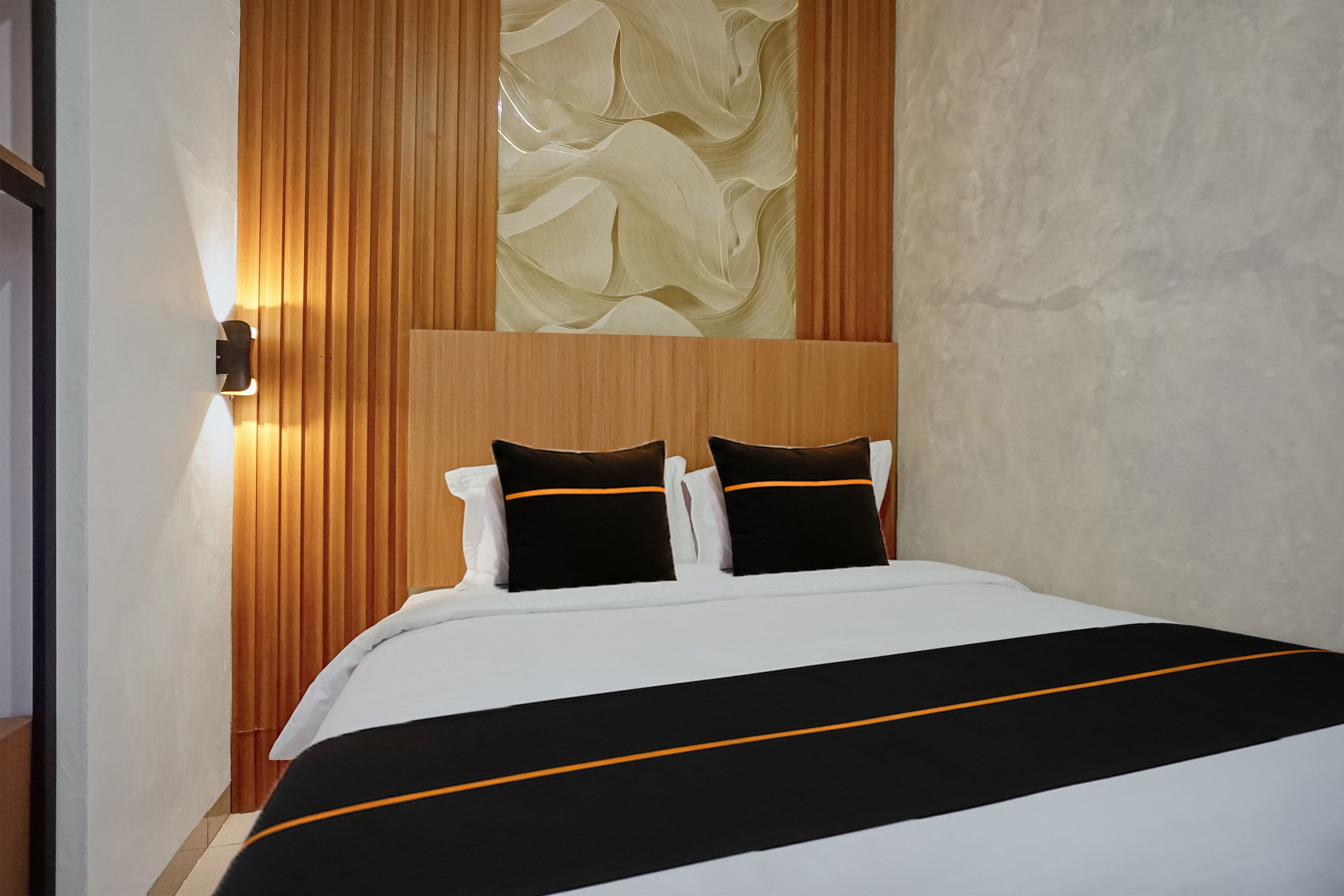 A hotel room with a bed, a wooden headboard, and a wall with a textured design.