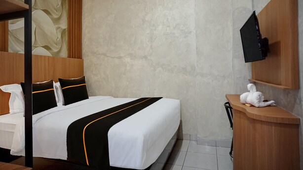 A hotel room with a bed, a television mounted on the wall, and a small table with a white object on it. - Hotel O near Universitas Sumatera Utara  (Medan)