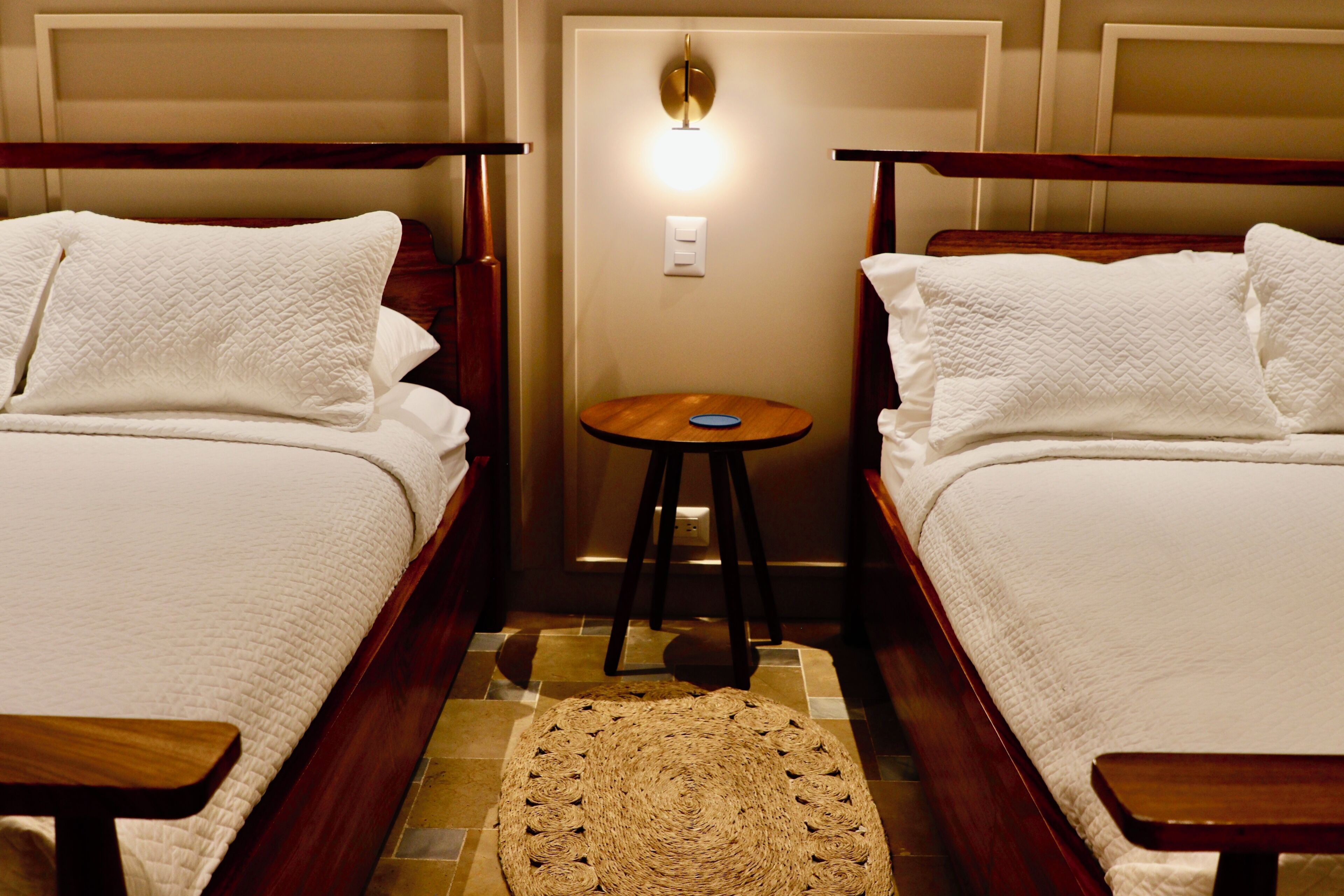 A hotel room with two beds, a small round table, and a wall-mounted light fixture.