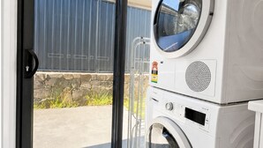 A laundry room with a large window, a metal drying rack, and stacked washing machines.