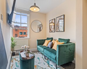 A cozy living room with a teal sofa, a round mirror, and abstract art on the wall. - Homely Stay | Fast Wi-Fi|Smart TV|Balcony (Birmingham)