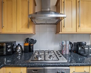 A kitchen with wooden cabinets, a stainless steel range hood, a gas stove, a coffee maker, and a toaster. - Homely Stay | Fast Wi-Fi|Smart TV|Balcony (Birmingham)
