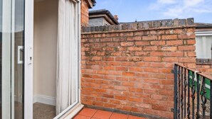 Un balcone con un muro in mattoni, una porta scorrevole in vetro e un recinto in metallo.