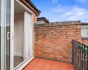 Un balcone con un muro in mattoni, una porta scorrevole in vetro e un recinto in metallo.
