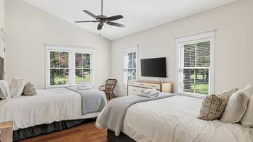 A bedroom with two beds, a ceiling fan, a TV, and large windows with blinds.