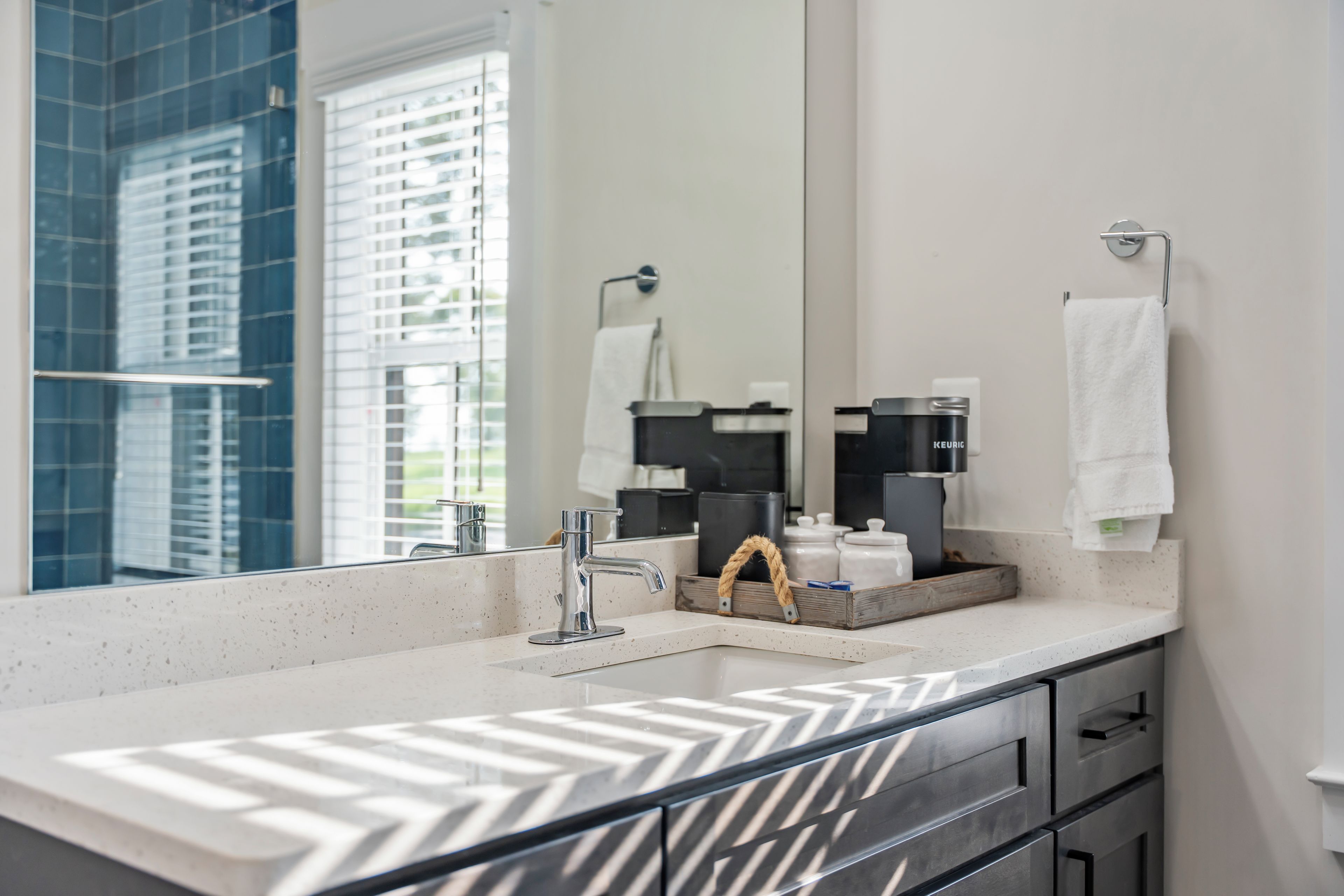 A modern bathroom with a large mirror, a white countertop, and a coffee maker.