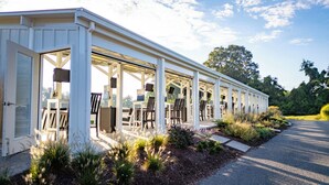 A covered outdoor seating area with tables and chairs, a pathway leading to it, and a landscaped garden.