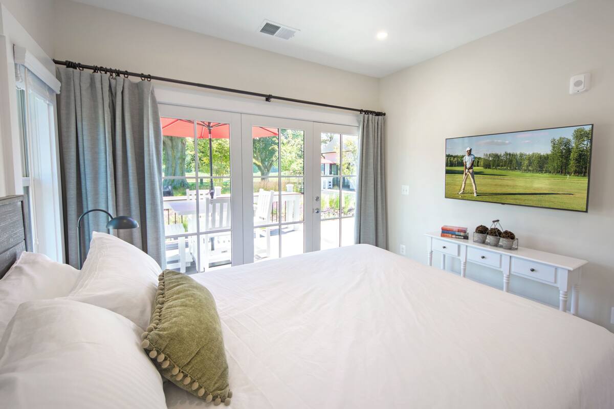 A bedroom with a large bed, a view of an outdoor patio, a mounted TV, and a small white dresser.