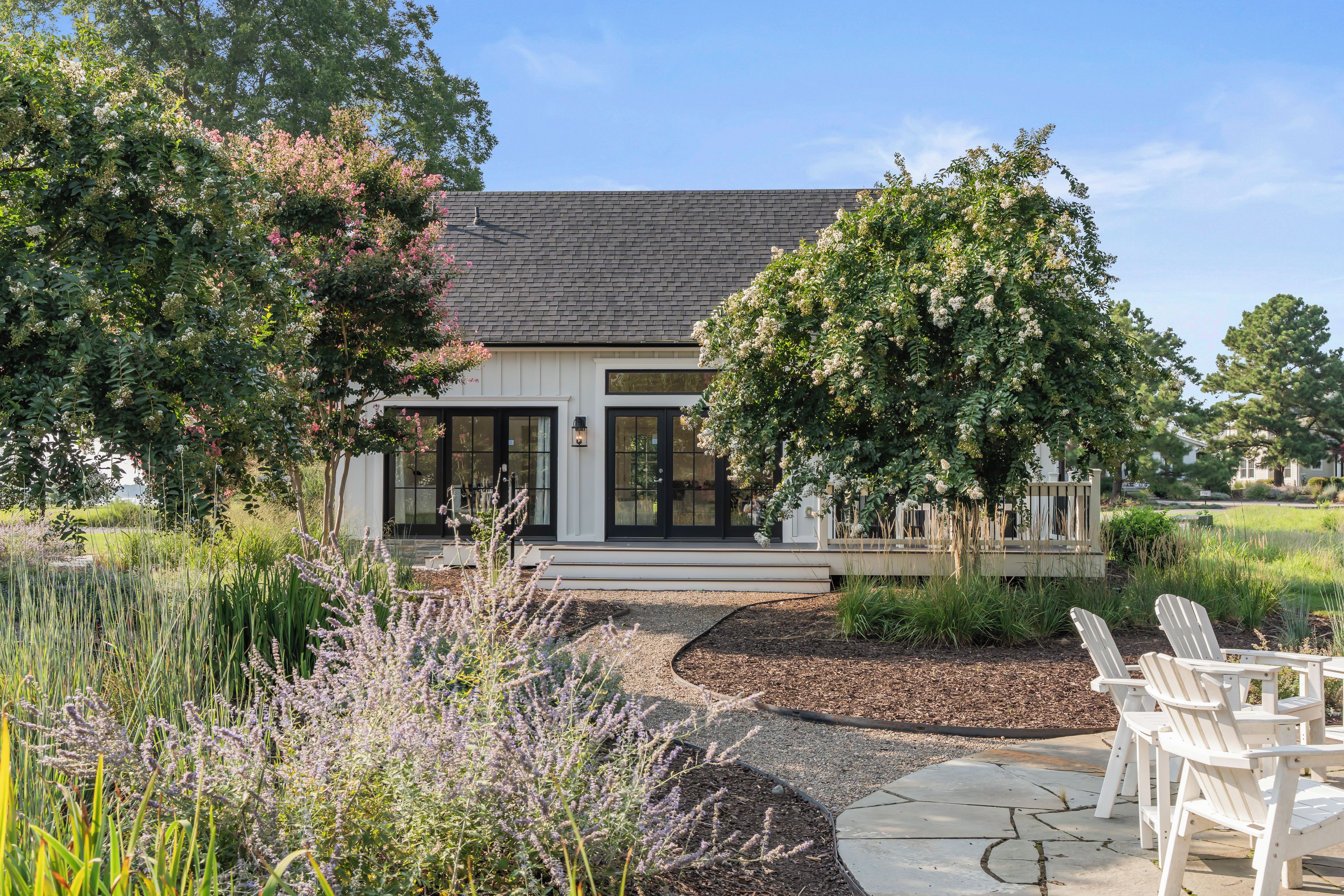 A modern house with a large front porch, a well-maintained garden, and outdoor seating.