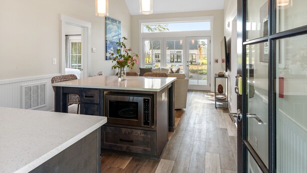 A modern kitchen with a large island, pendant lights, and a view to the outside.