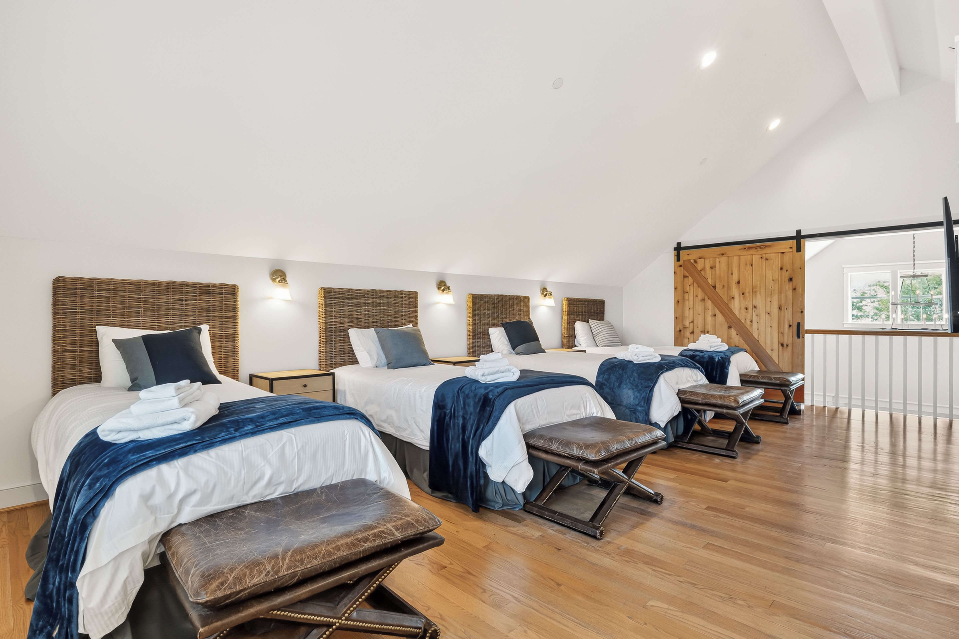 Habitación de hotel con tres camas, suelo de madera y un ventanal grande.