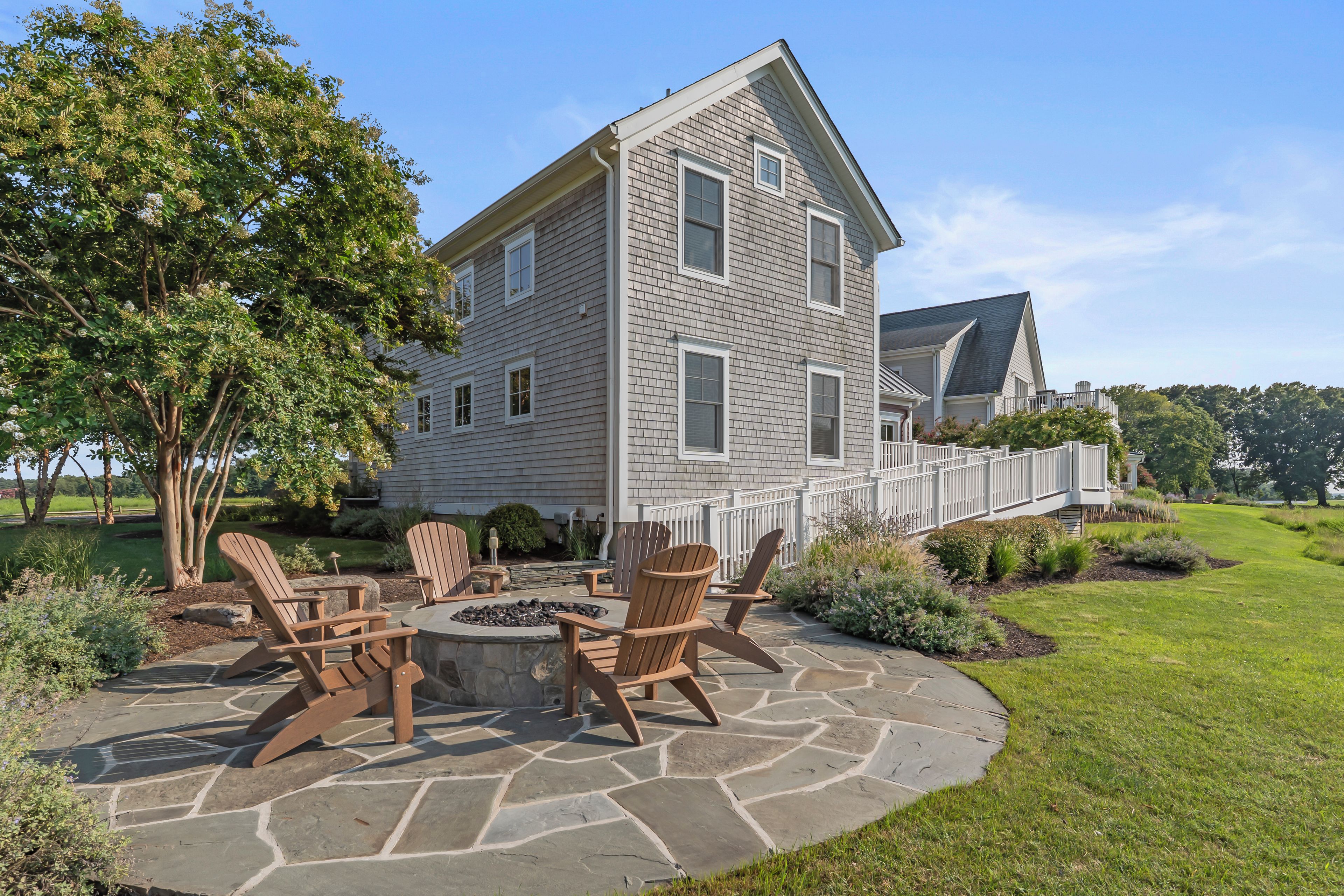 A two-story house with a stone patio, outdoor seating, and a fire pit.