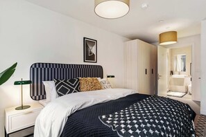 A modern bedroom with a bed, bedside table, lamp, and a view of the bathroom. - Apex Executive Apartments- The Ironworks (Dublin)