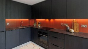 A modern kitchen with dark cabinetry, a central island, and a red backsplash. - Apex Executive Apartments- The Ironworks (Dublin)