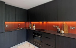 A modern kitchen with dark cabinetry, a central island, and a red backsplash. - Apex Executive Apartments- The Ironworks (Dublin)