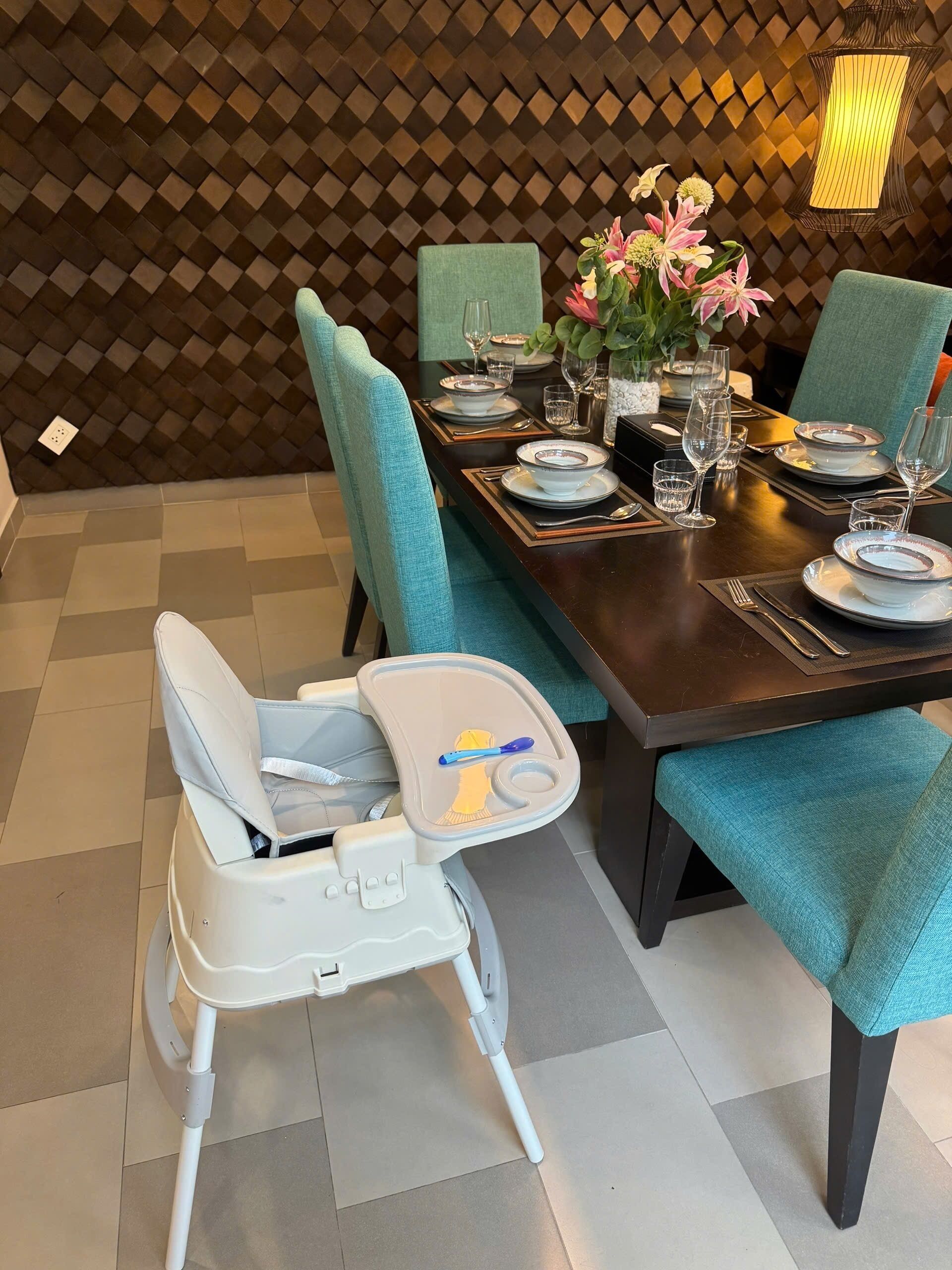 A dining area with a high table set for a meal, a child’s high chair, and a decorative wall.