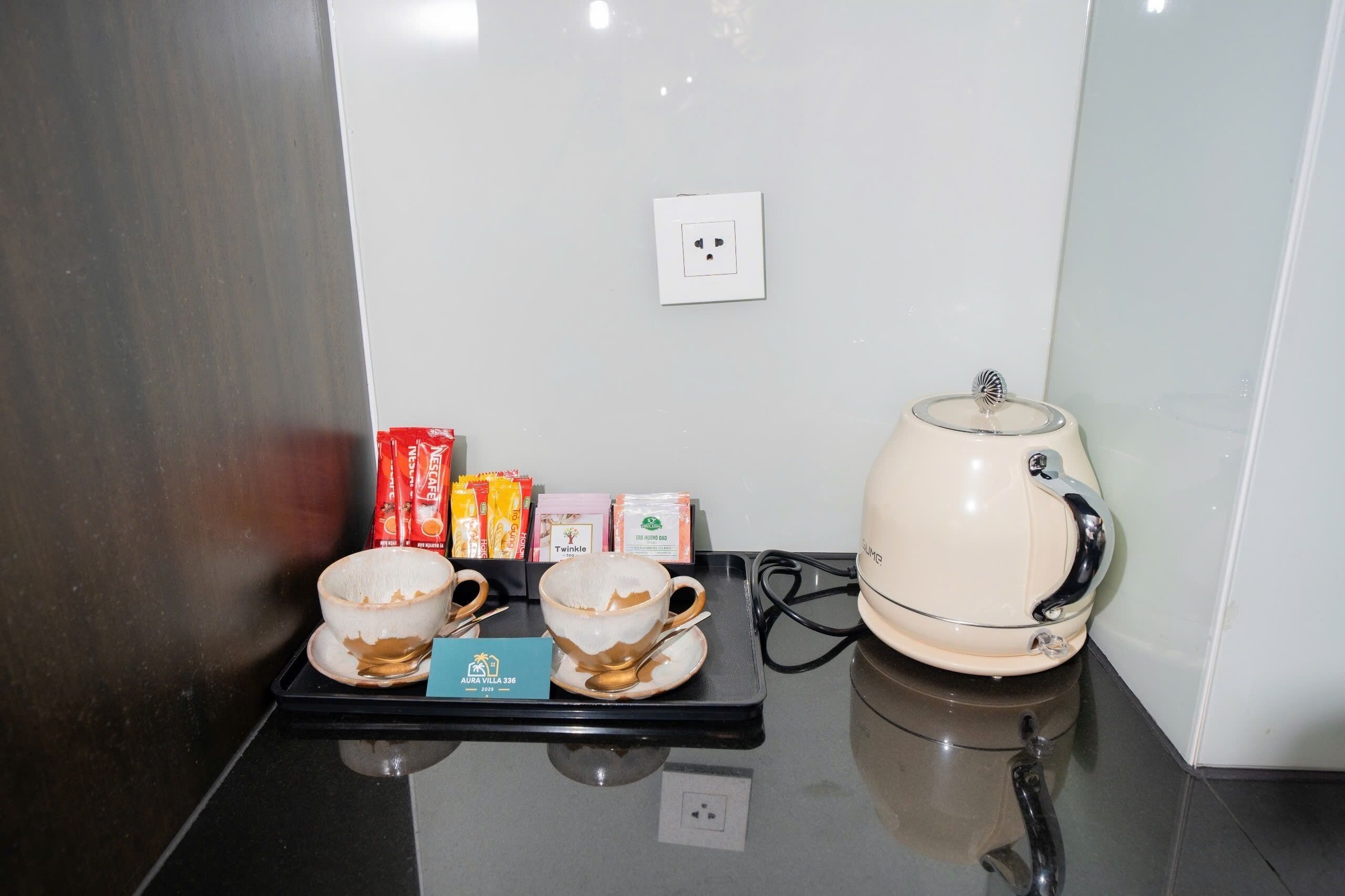 Una kitchenette con cafetera, dos tazas y una bandeja con cápsulas de café y una caja.