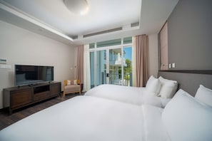 A hotel room with a large bed, a TV on a wooden cabinet, a small chair, and a balcony with curtains.