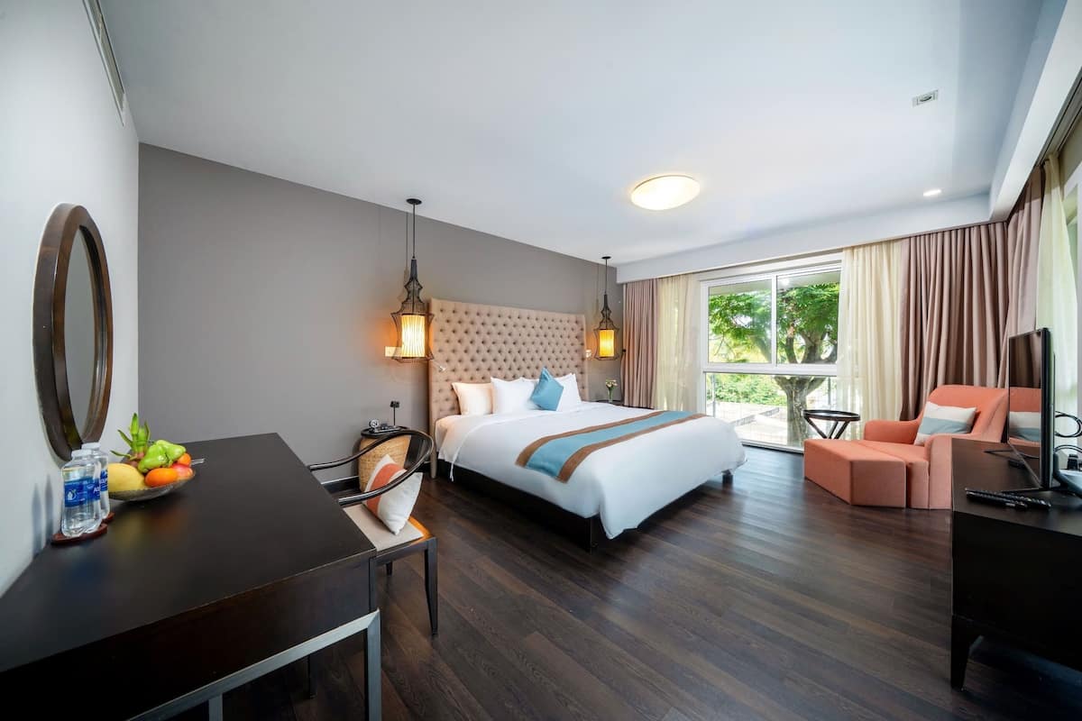 A hotel room with a bed, a desk with a fruit bowl, a chair, a sofa, and a TV.