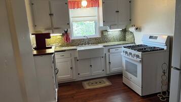 A compact kitchen with white cabinets, a stove, and a window with a red valance.