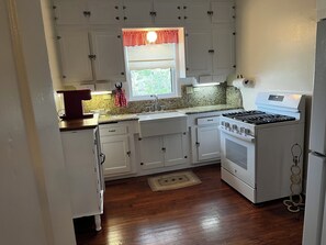 A compact kitchen with white cabinets, a stove, and a window with a red valance.