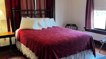 Un lit bien fait, avec une couvre-lit rouge et des oreillers blancs, un plancher en bois, un ventilateur de plafond et une fenêtre avec des rideaux.