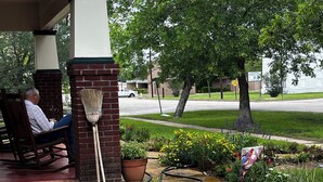 A covered outdoor seating area with a brick column, a broom, and potted plants.