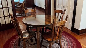 A dining area with a round table, four wooden chairs, a red and gray woven rug, and a wooden door with a glass panel.