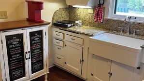 A kitchen with white cabinets, a red coffee maker, a granite countertop, and a window with a view of greenery.