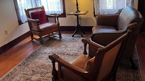 A living room with two wooden chairs, a small table with a lamp, and a patterned rug.
