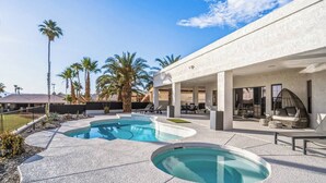 Et moderne poolområde med en rund pool, liggestole og palmer.