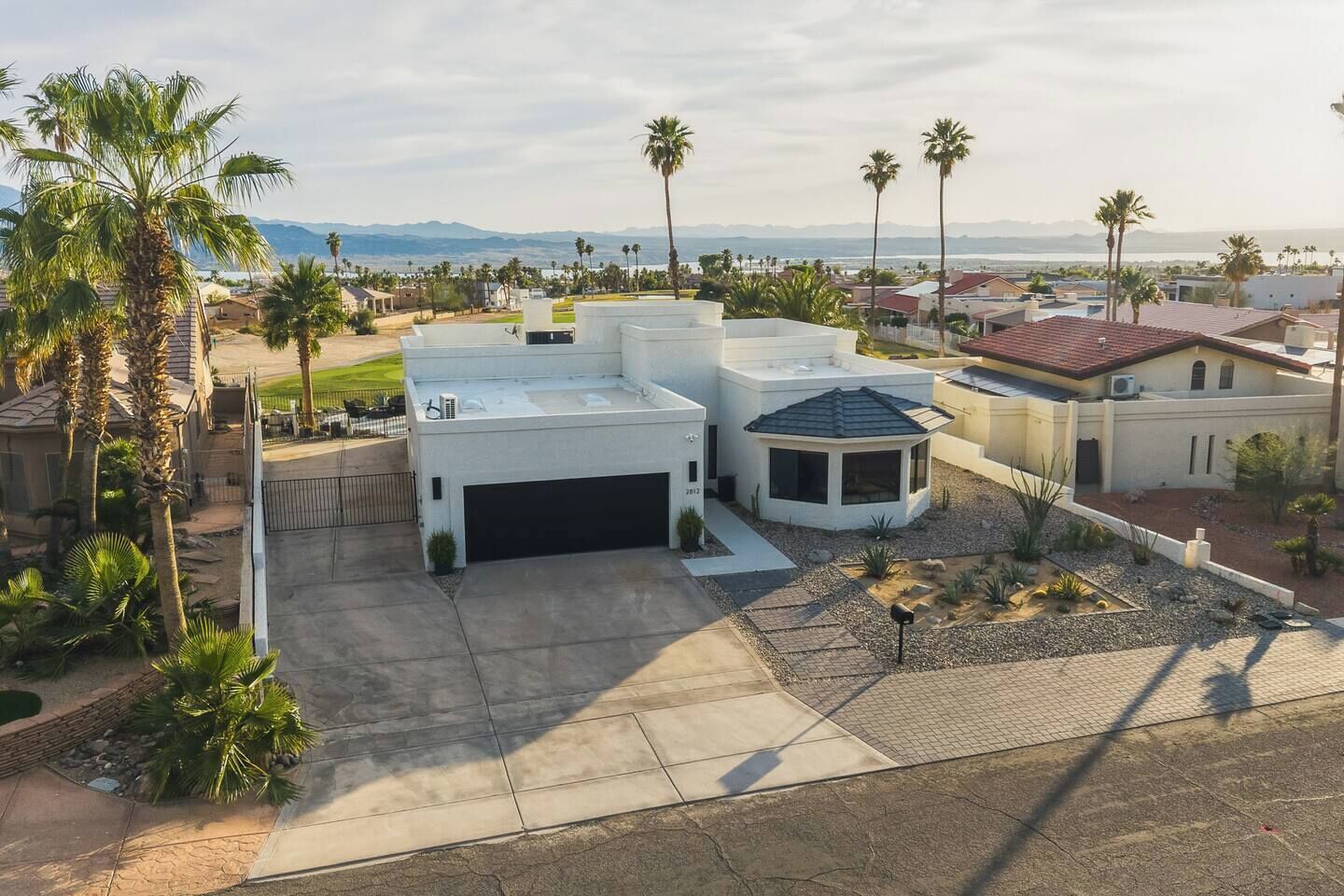 A modern house with a garage, a small garden, and palm trees.