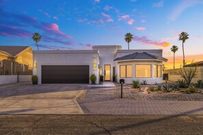 Ein modernes, zweistöckiges Haus mit Garage, überdachter Terrasse und einem angelegten Vorgarten mit Wüstenpflanzen.