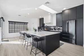 Eine moderne Küche mit Kochinsel, Barhocker, dunklen Schränken und einem großen Kühlschrank.